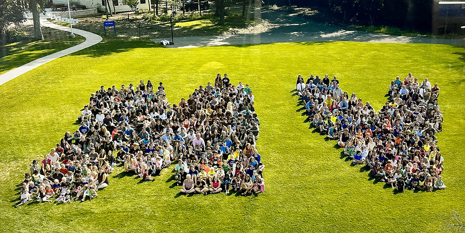students sitting in grass in the shape of MV